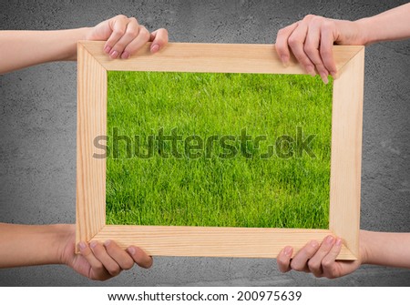 Close up of human hands holding wooden frame with green grass
