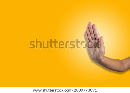 A hand showing an obstructing gesture, with an open palm facing forward on a yellow background. Royalty-Free Stock Photo #2009773091