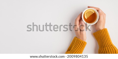 First person top view photo of female hands in yellow sweater touching white cup of tea with lemon slice on isolated white background with copyspace Royalty-Free Stock Photo #2009804135
