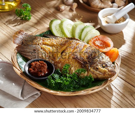 "Ikan Gurame Goreng" or fried freshwater fish with chilli sauce and vegetable. Serving on wooden table. Indonesian food and cuisine.  Royalty-Free Stock Photo #2009834777