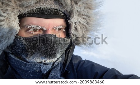 Traveler in the Arctic. Portrait of a freezing man in winter clothes, a hood and a warm mask. Ice on the eyebrows and eyelashes. Extremely cold weather in the far north in the Arctic. Face close-up. Royalty-Free Stock Photo #2009863460
