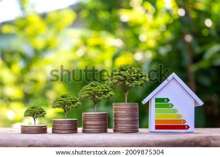 Trees grow on piles of money and energy-saving charts on home models in a residential home energy efficiency assessment concept office. Royalty-Free Stock Photo #2009875304
