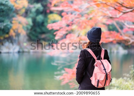 Happy woman tourist looking colorful leaves and Katsura river in Arashiyama, young Asian traveler visit in Kyoto and enjoy travel in Japan. Fall Autumn season, Vacation,holiday and Sightseeing concept