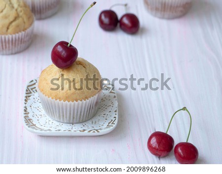 homemade fresh muffin decorated with fresh cherries stands on a saucer on a wooden background. Cherry muffin close-up. Cherry with a root lies on a cupcake. High quality photo