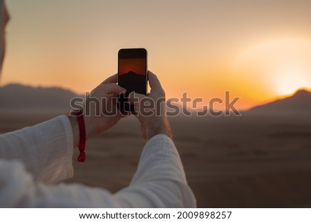 Male hands holding mobile phone with image of sunset or sunrise on the screen, taking photo