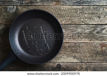 Empty fry pan over wooden background. Top view, copy space. Dark grey culinary background. Man pouring cooking oil on the frying pan.