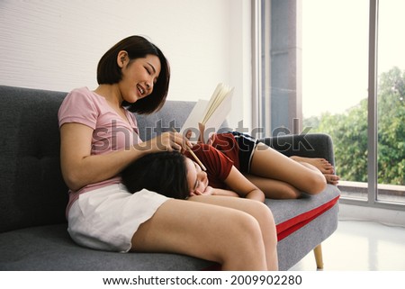 A couple of lovely woman writing diary and holding book while smiling and looking eyes on sofa. They are happiness and building good relationships in the future.