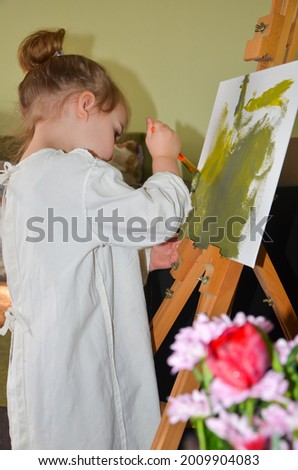 photo little girl artist, child draws a picture on canvas in the house