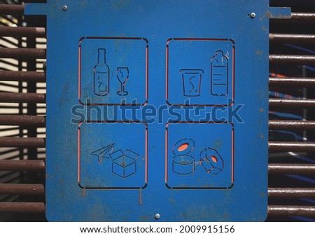 Images of different types of garbage on a container for recyclable materials. Symbols of glass, plastic, paper and metal waste types. Outdoor shot on a sunny day. 