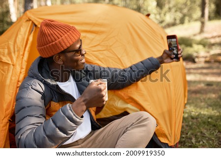 Guy posing for selfie, holding cup of drink. Making memories or send picture to family. Camping in forest after hiking in mountains. Nature, travelling alone, enjoy life concept