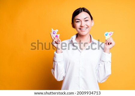 Happy asian girl in shirt holding pop it and simple dimple while standing on yellow background