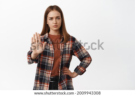 Enough, stop. Young woman looks exhausted and raise hand in block, say no, refuse prohibit or reject smth disappointing, telling to stay away, standing against white background Royalty-Free Stock Photo #2009943308