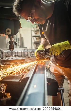 Man working with electric grinder tool on steel structure in factory, sparks flying. Grinding machine in action