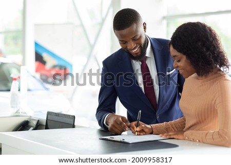 Happy Black Woman Buying New Car, Signing Papers With Male Salesman In Dealership Office, Cheerful African American Female Driver Purchasing New Automobile In Modern Showroom, Copy Space