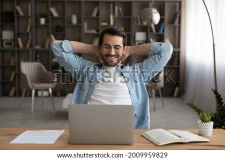 Happy young man worker in eyeglasses relaxing on chair with folded hands behind head, enjoying break pause time during working day or finishing online project on computer in modern home office. Royalty-Free Stock Photo #2009959829