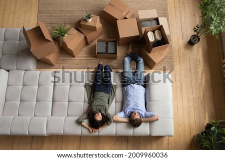 Ready to relocate. Top view of loving young married couple sit relax on cozy couch after packing stuff. Happy spouses resting on sofa waiting for transportation service to move things to new dwelling Royalty-Free Stock Photo #2009960036