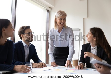Happy mature mentor working with group of new employees in office, training interns in boardroom, speaking before audience, smiling, laughing. Senior business leader discussing project with managers Royalty-Free Stock Photo #2009960048