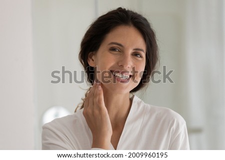 Young hispanic female with perfect healthy white smile pose for portrait in bathroom touch neck enjoy morning daily spa procedures. Happy beautiful millennial woman look at camera take care of skin Royalty-Free Stock Photo #2009960195