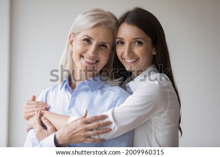 Happy young grownup daughter hugging mature mother, looking at camera, smiling, Affectionate cheerful millennial girl embracing senior 60s grandma. Family relationship concept. Head shot portrait