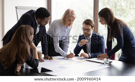 Serious senior mentor, corporate teacher training interns. Business coach, leader, boss teaching employees to analyze project documents, reviewing reports, using scrum method with sticky notes Royalty-Free Stock Photo #2009960414
