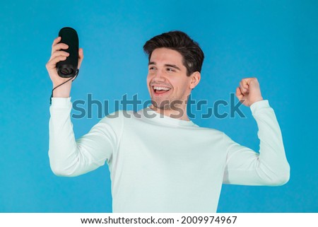 Man listening to music by wireless portable speaker - modern sound system. Young guy dancing, enjoying at blue studio background. He moves to the rhythm of music
