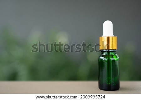 A green glass bottle with dropper on the table. Concept of aroma oil, cosmetic, and beauty skin.