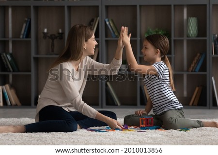 Happy millennial mom giving high five to cute little daughter kid, celebrating success in building game, playing with construction blocks on heating floor with carpet, enjoying home activity together Royalty-Free Stock Photo #2010013856