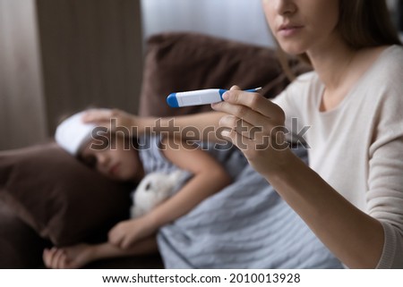 Worried mom treating sick kid suffering from flu and fever, holding thermometer, checking high body temperature, applying cold compress on forehead. Childcare, kids healthcare concept Royalty-Free Stock Photo #2010013928