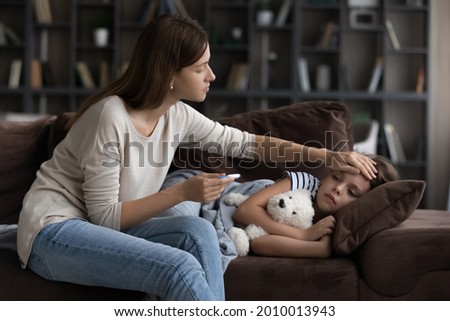 Concerned mother checking high body temperature of daughter, touching head, forehead, holding thermometer. Sad sick girl lying on sofa, suffering from influenza, fever. Children healthcare concept Royalty-Free Stock Photo #2010013943