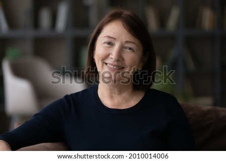 Portrait of happy senior mature woman in casual sitting on couch at home, looking at camera, smiling. Head shot of middle aged 60s lady, satisfied older customer video call screen view Royalty-Free Stock Photo #2010014006