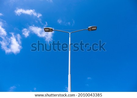 Lamp post with bright blue sky and some clouds. Royalty-Free Stock Photo #2010043385