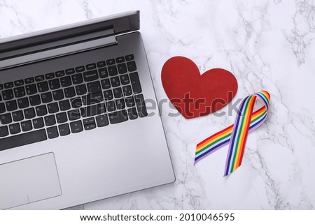 Laptop, LGBT rainbow ribbon pride tape symbol and heart on marble background.