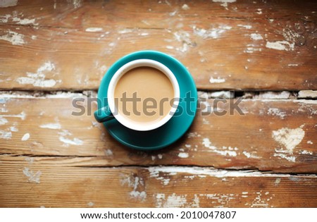 Top view studio photo of hot coffee with milk in blue porcelain cup and saucer on vintage wooden surface with copy space for text, photo in rustic style