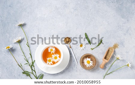 Healthy flat lay with chamomile tea in a white cup, vase, dry tea and  flowers daisy  on a blue background. Top view and copy space image 