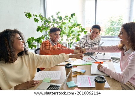 Young happy laughing creative startup team four multiethnic coworkers diverse students work together give fist bump celebrate successful project in office classroom at desk. Teamwork success concept. Royalty-Free Stock Photo #2010062114