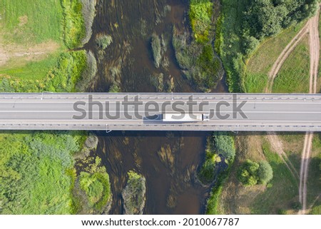 Aerial top down view of truck driving over bridge. River flowing under bridge
