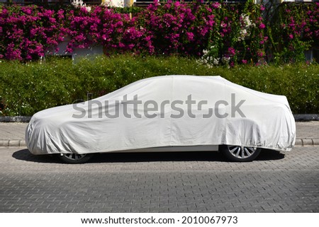 a parked car covered with a sun protection fabric on the street of green city Royalty-Free Stock Photo #2010067973