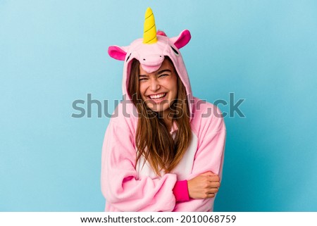 Young caucasian woman wearing a unicorn pajama isolated on blue background laughing and having fun.