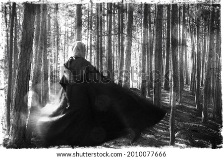  A medieval cloaked woman moving through a forest. Creative ghostly black and white photo.  Witch, shamanic theme.  Royalty-Free Stock Photo #2010077666