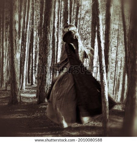  A mysterious cloaked woman moving through a forest. Creative ghostly black and white photo. Shamanic theme. Royalty-Free Stock Photo #2010080588