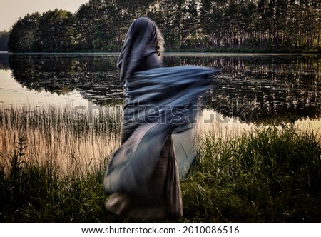  A medieval dressed woman moves through a marsh overlooking early morning mystical lake. Creative haunting colors. Royalty-Free Stock Photo #2010086516