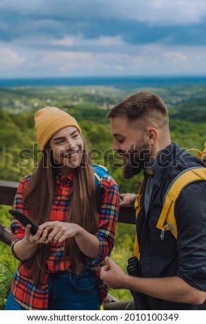 Couple of hikers using smartphone for a orientation while wearing backpacks with a camping gear and spending time in the nature