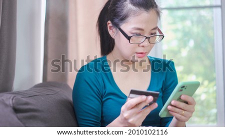 Woman shopping on mobile phone with Credit card while sitting on the sofa at home