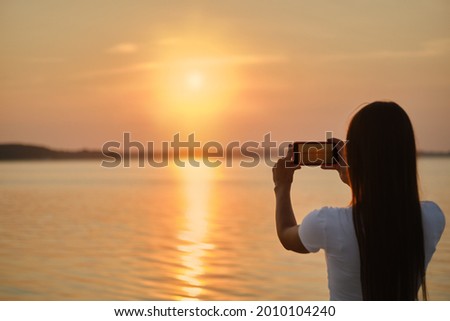 Young woman making photo of sunset with her smartphone