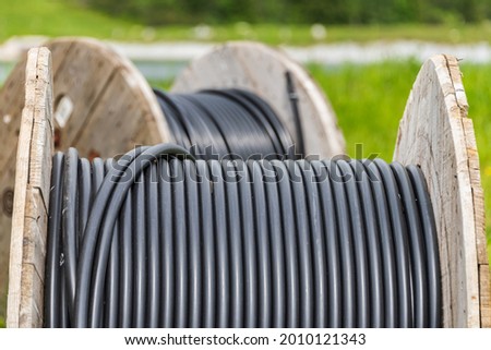 Large wooden cable pulleys with electric cables. Cable reels, cable drums lying on the construction site. In the background, the blue sky and mountains covered with green vegetation Royalty-Free Stock Photo #2010121343