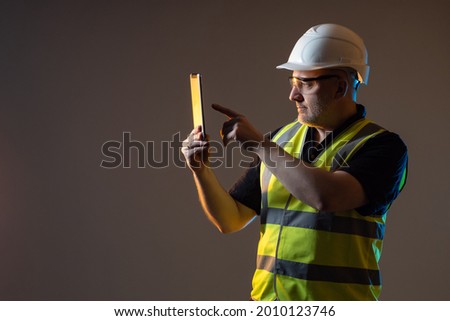 Builder photographs something on phone. Concept - he makes a photo report on work done. Builder with a smartphone on a dark background. Engineer or architect in a work uniform. Work as architect