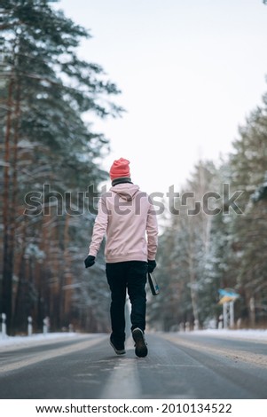 Guy standing on the road in the middle of the forest, surrounded by snow