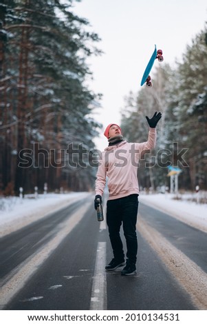 Skateboarder standing on the road in the middle of the forest, surrounded by snow