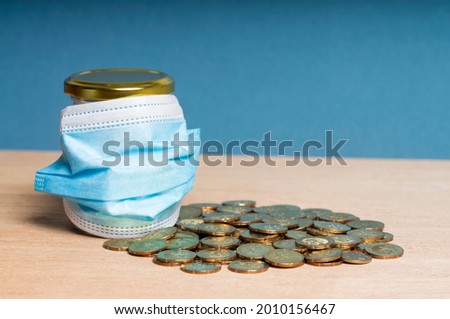 COVID-19 ECONOMIC CRISIS. Face mask and gold coins on blue background