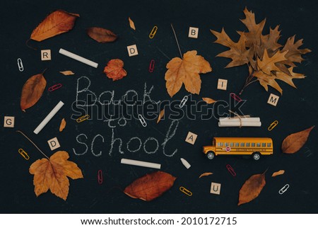 Back to school concept with school bus, chalk, leaves, letters and paper clips on black background, top view close-up.